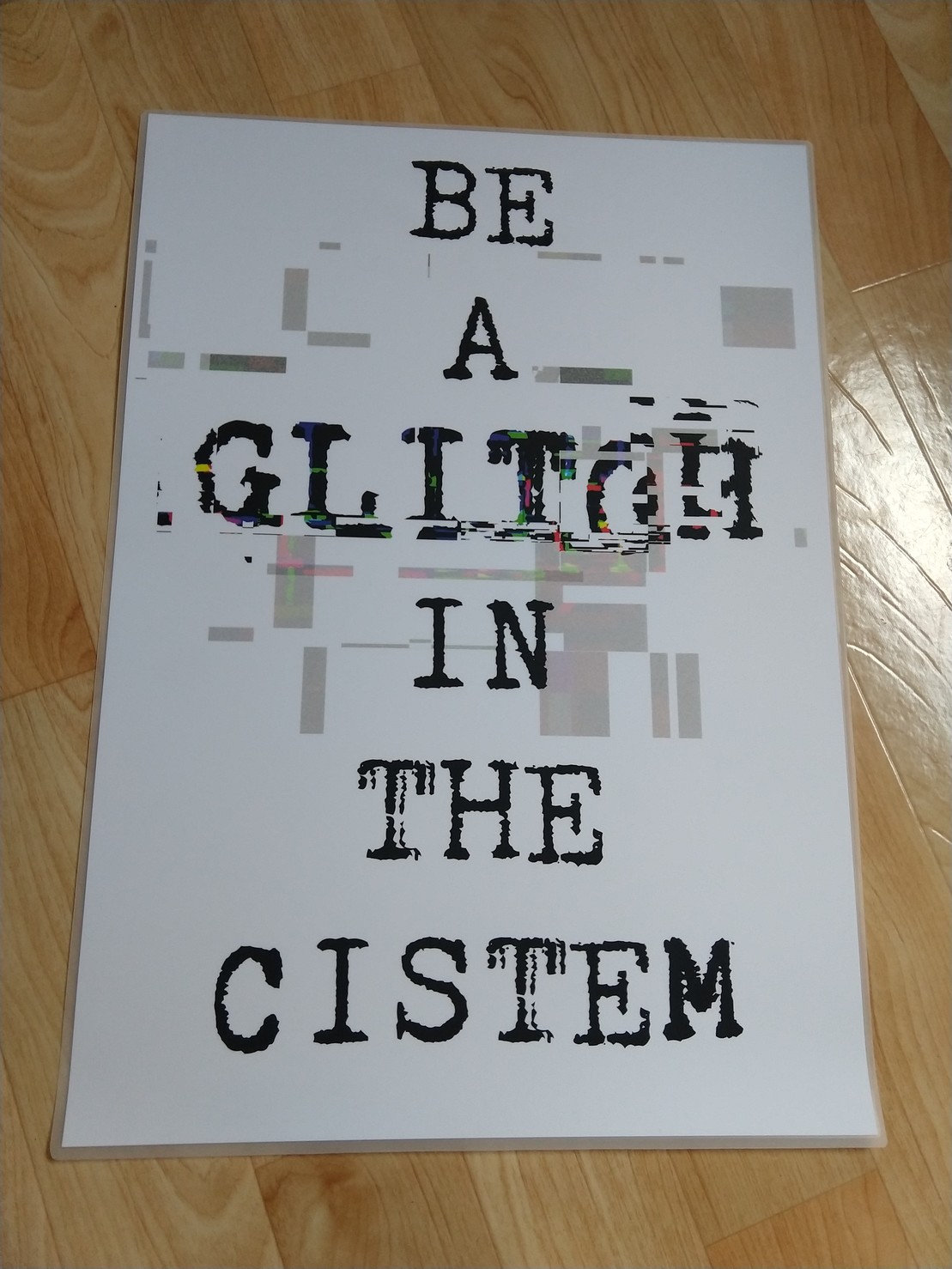 Image of my poster. It says “BE A GLITCH IN THE CISTEM” and the word glitch is  creatively distorted, ie. “glitched”. The whole thing is also laminated.